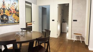 Un'area pranzo con un tavolo rotondo e sedie, un quadro appeso al muro, e vista su cucina e bagno.