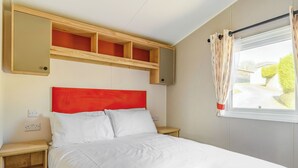 A single bed with a red headboard, wooden nightstands, a mirror above the bed, and a window with curtains. - Ocean Wave Plus (Pets Welcome) (Woolacombe)