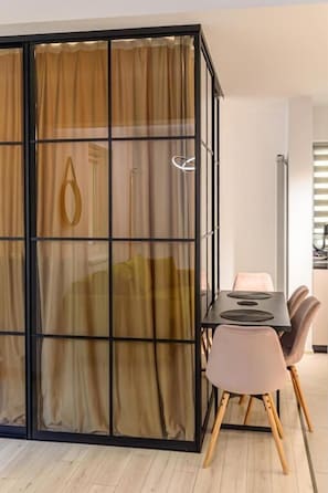 A modern dining area with a table and chairs, a partition with curtains, and a glimpse of a kitchen area.