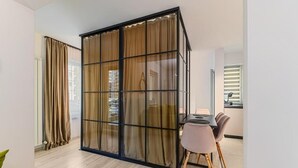 Ένα μοντέρνο δωμάτιο με μια συρόμενη γυάλινη διαχωριστική πόρτα, ένα τραπέζι φαγητού με καρέκλες και θέα στον εξωτερικό δρόμο.
