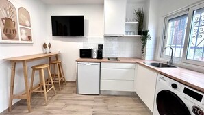 Una cucina compatta con lavastoviglie, forno a microonde, lavello e lavatrice. Sono presenti sgabelli di legno e un piccolo tavolo.
