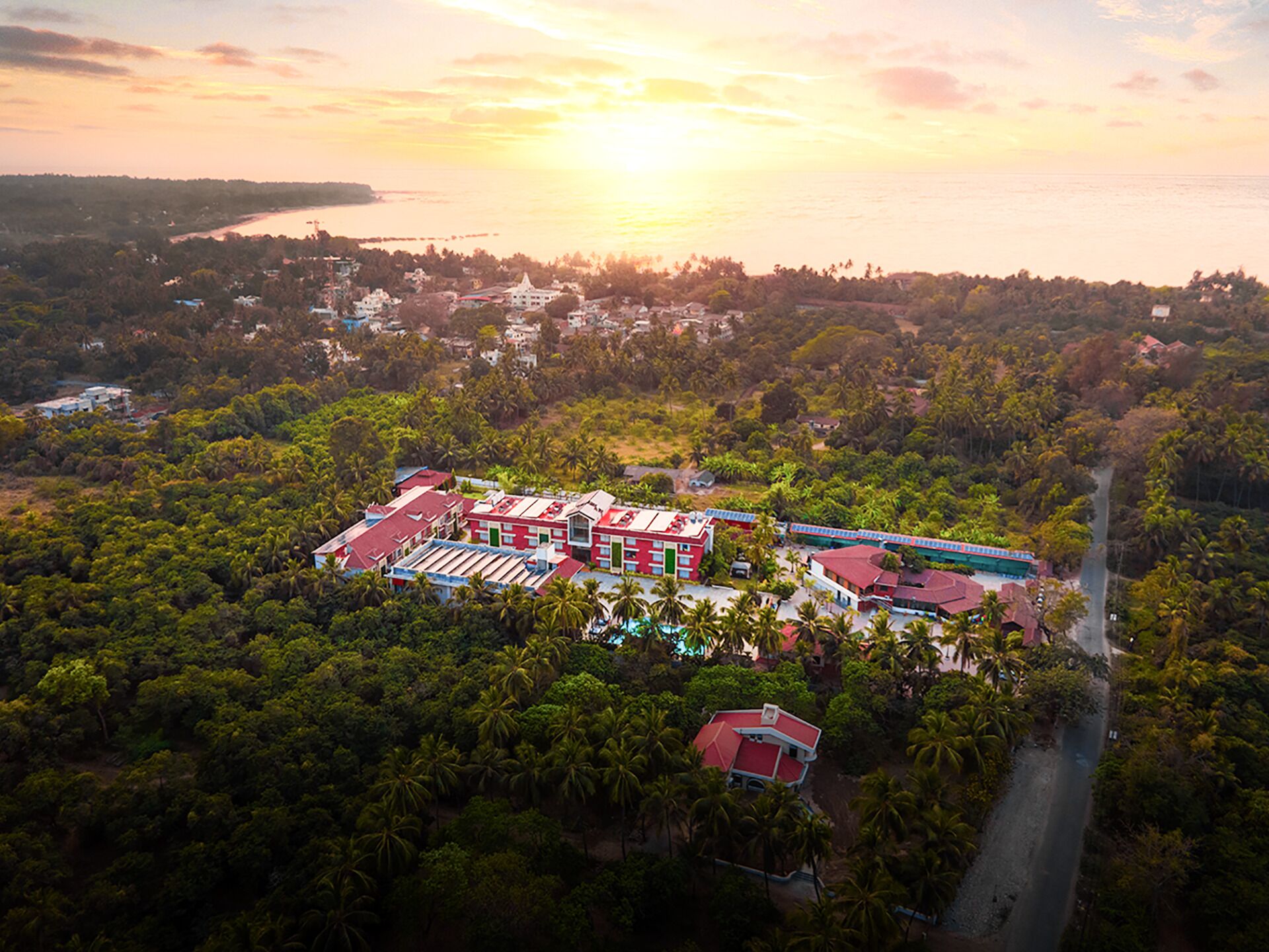 An aerial view of a resort with multiple buildings, surrounded by dense tropical vegetation and a body of water.