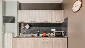 Een moderne keuken met lichte houten kastjes, een zwarte spatwand, een magnetron, een waterkoker en een klok aan de muur.