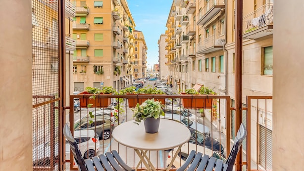 Een balkon met een tafel en stoelen, met uitzicht op een straat met geparkeerde auto's en gebouwen.