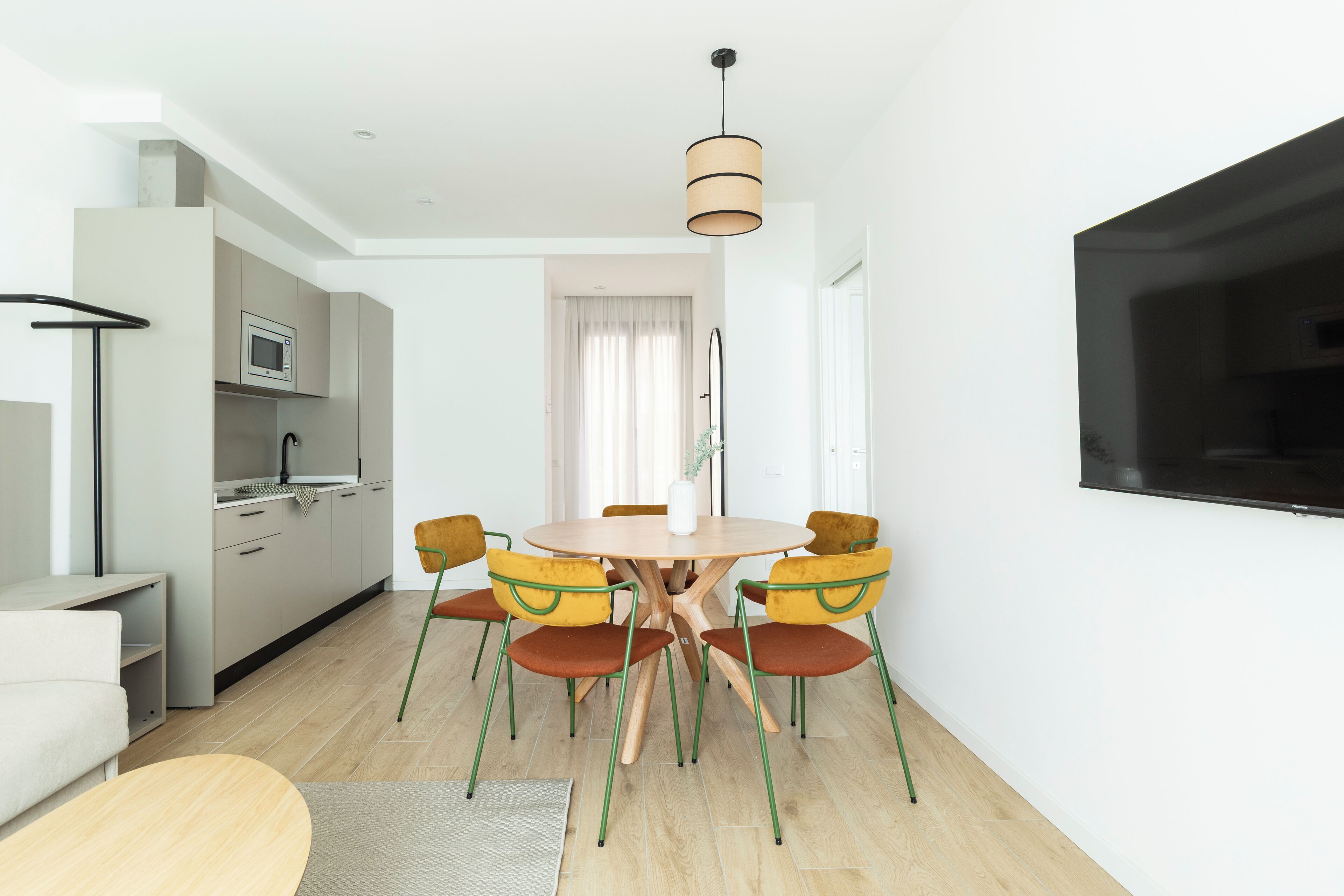 A modern kitchen with a dining area, a flat-screen TV, and a minimalist design.