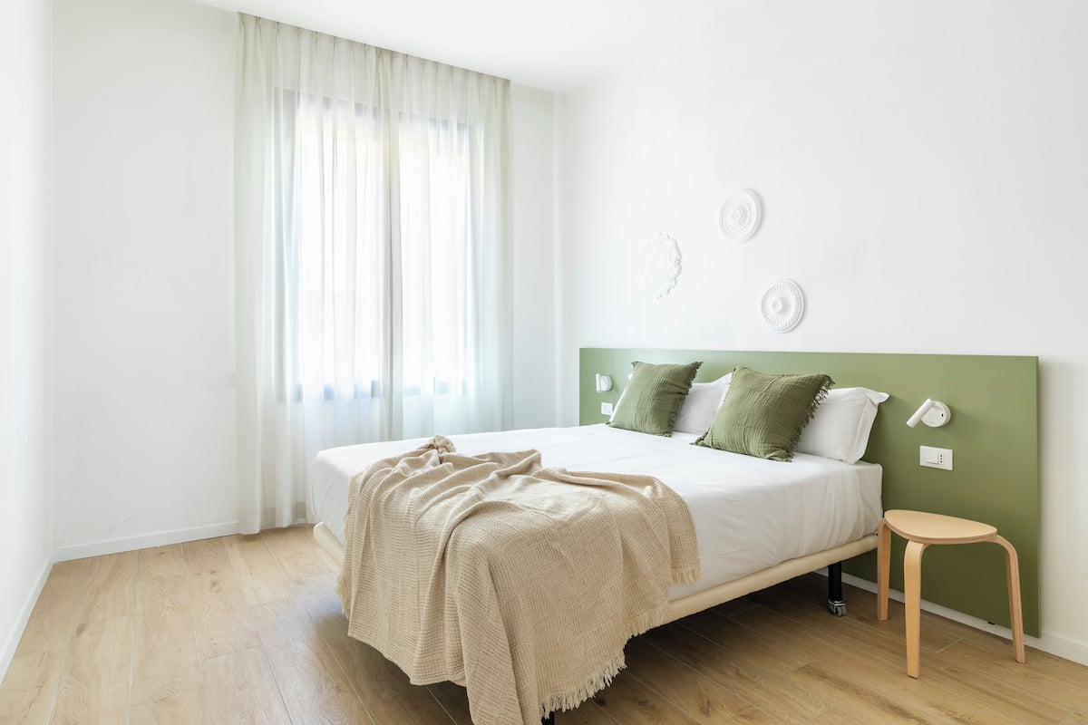 A bedroom with a bed, a bedside table, a window with curtains, and wall decor.