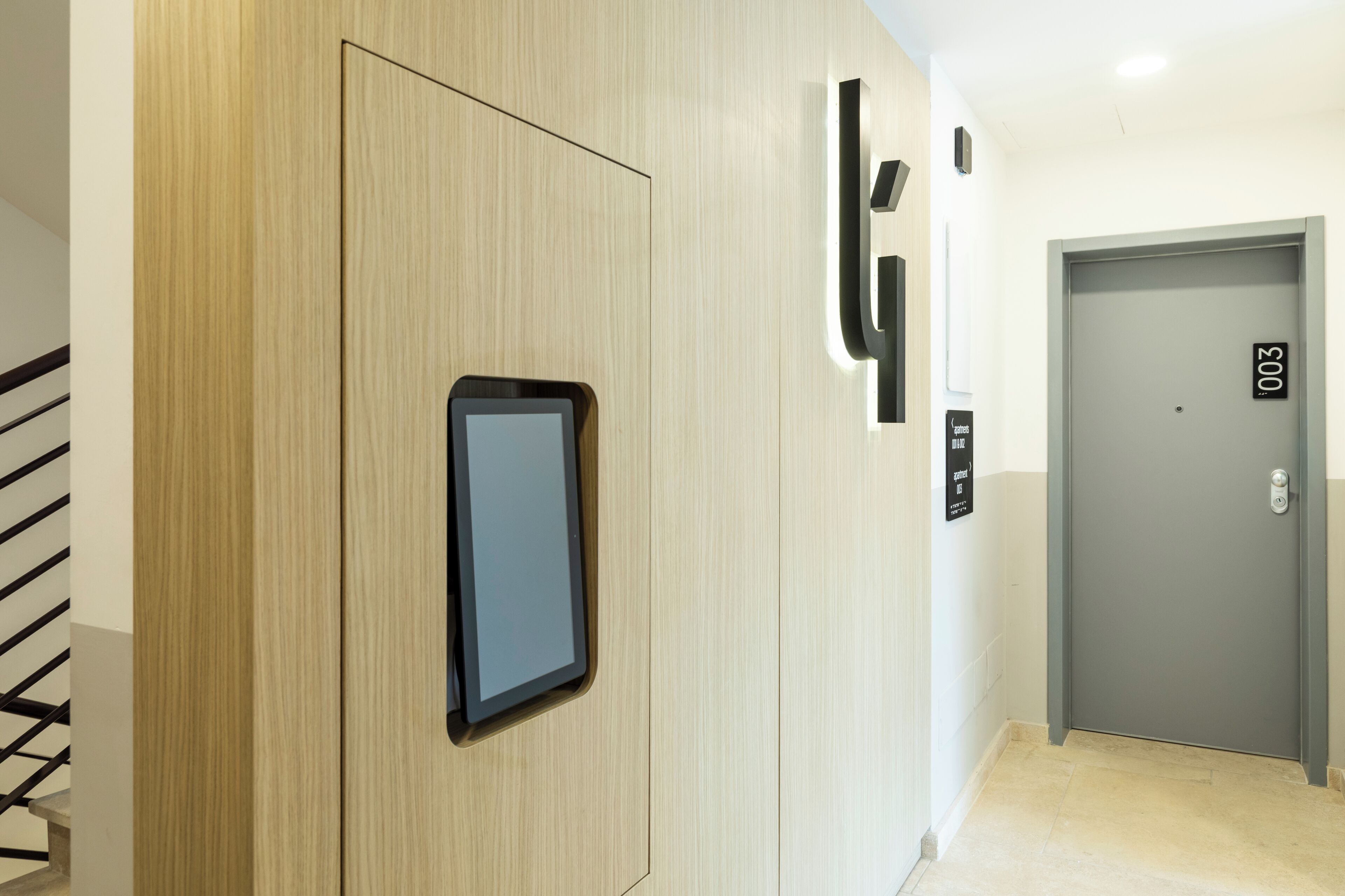 Un ascensor moderno con pantalla digital, un revestimiento de pared de madera y una puerta gris con placa numérica.