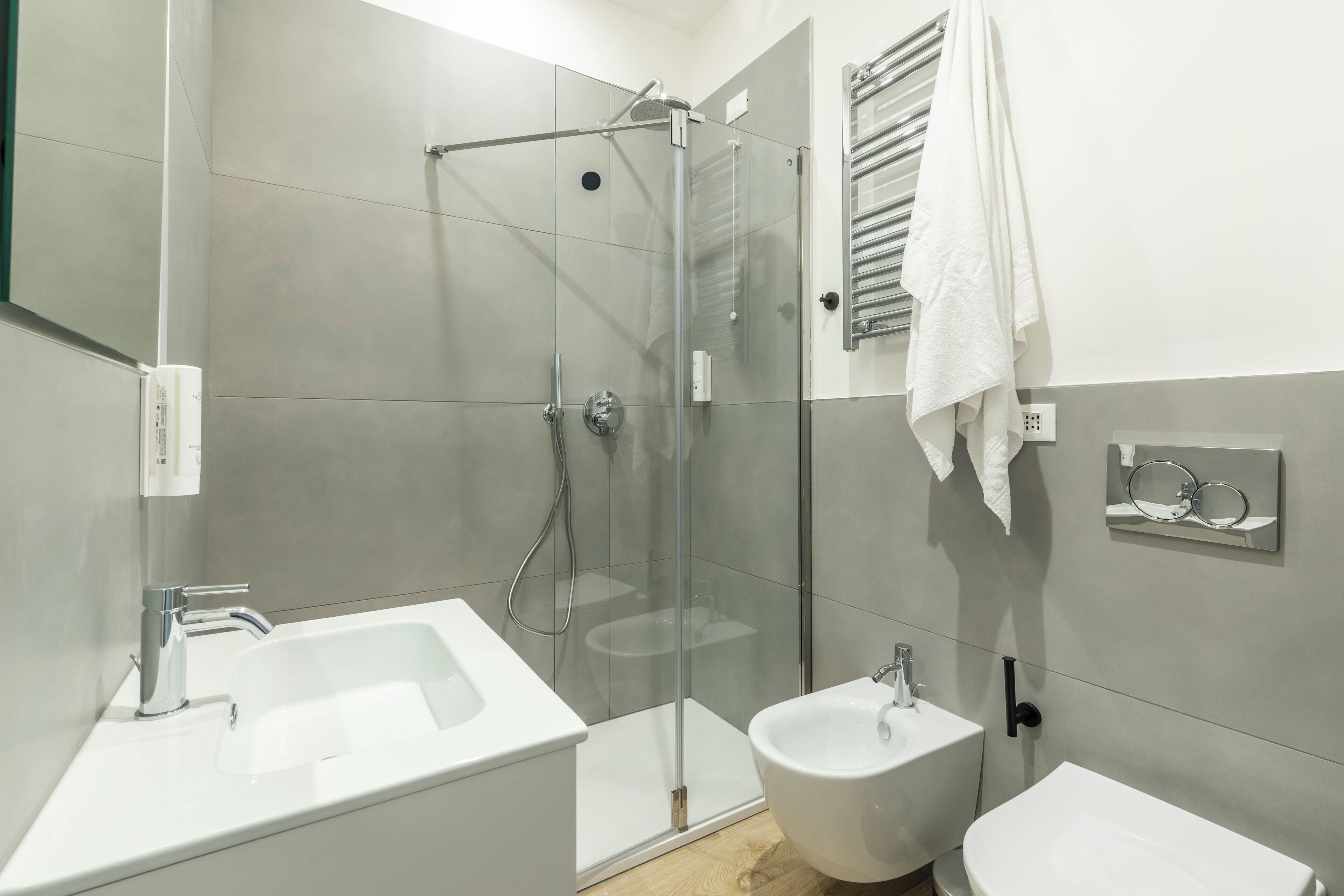 A modern bathroom with a glass-enclosed shower, a large sink, a bidet, and a mirror with a towel rack.