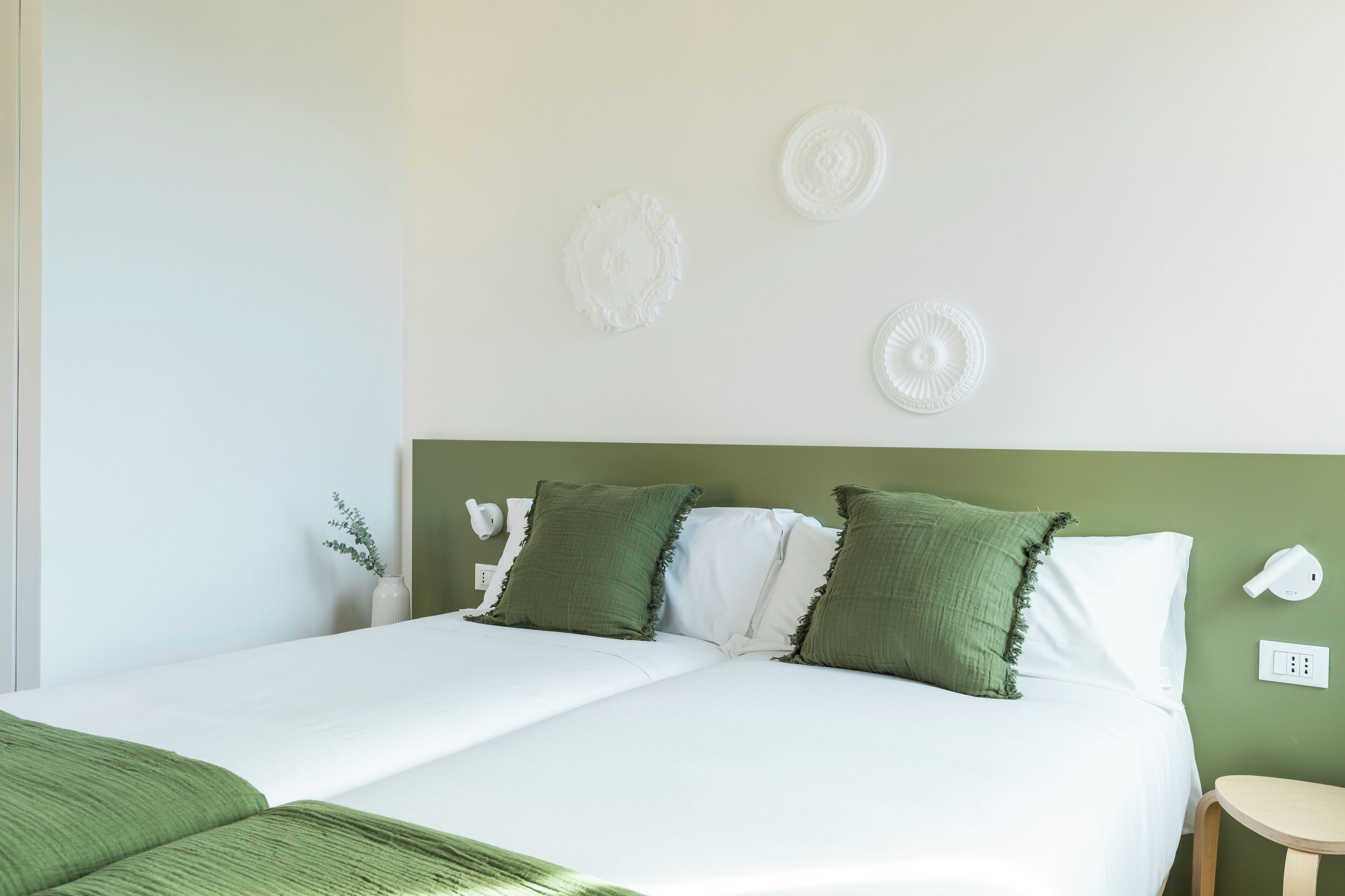 Een opgemaakt bed met groen-witte beddengoed, een groen hoofdeinde en decoratieve wandkunst.