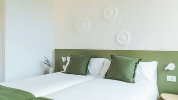 Een opgemaakt bed met groen-witte beddengoed, een groen hoofdeinde en decoratieve wandkunst.