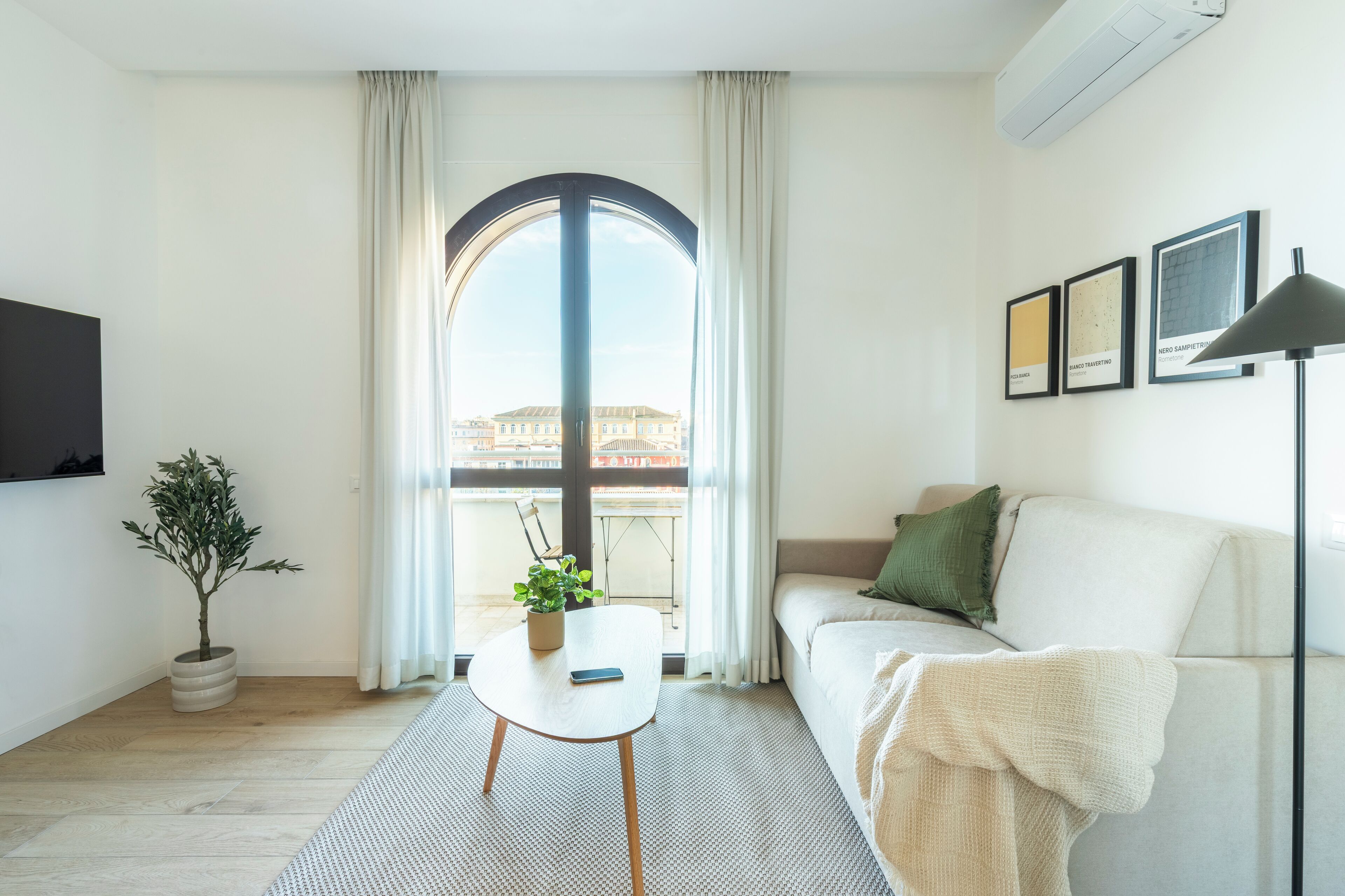A modern living room with a large window, a sofa, a small table, and a potted plant.