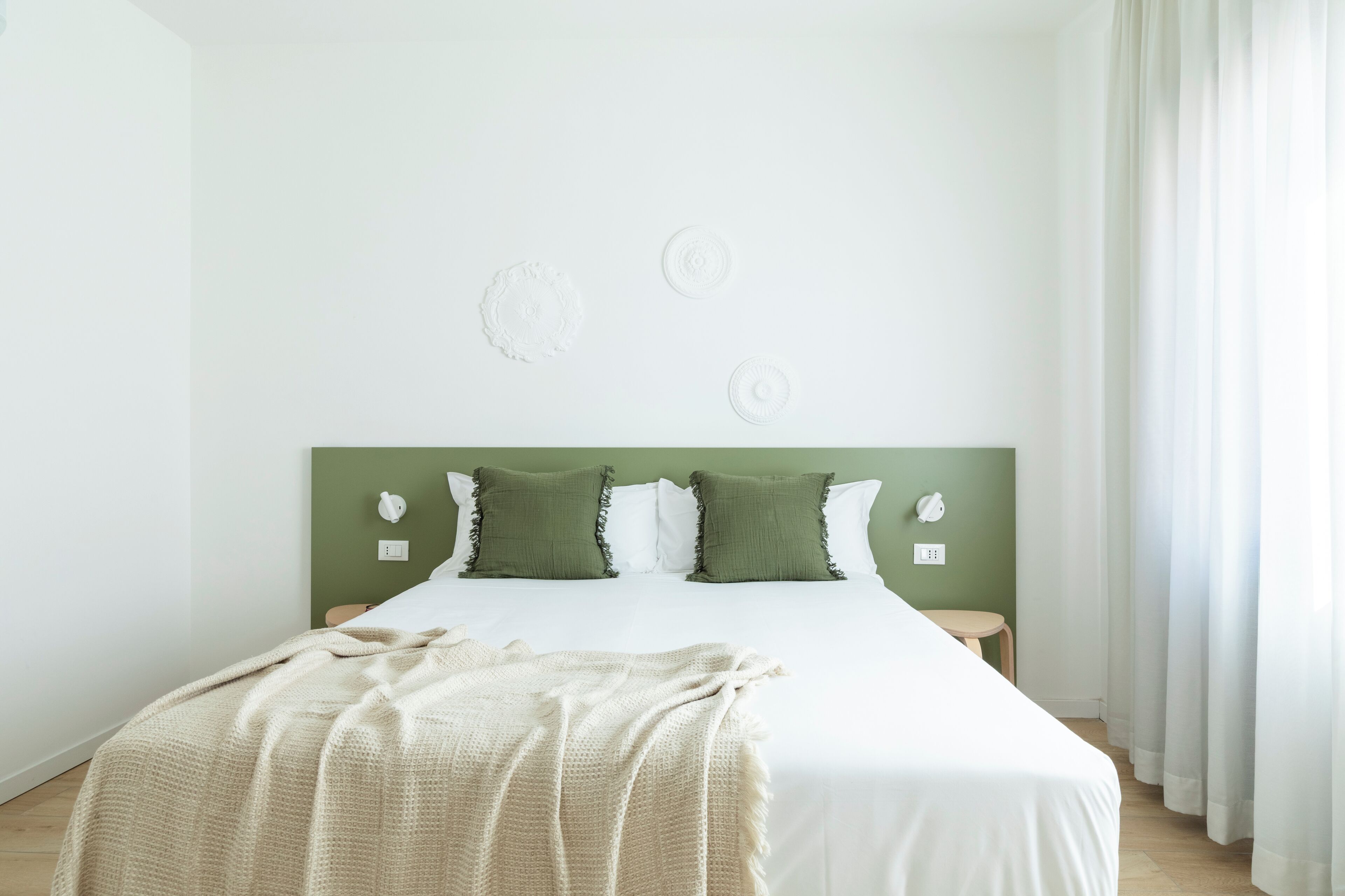 A neatly made bed with a white and beige blanket, two green pillows, and a green headboard.