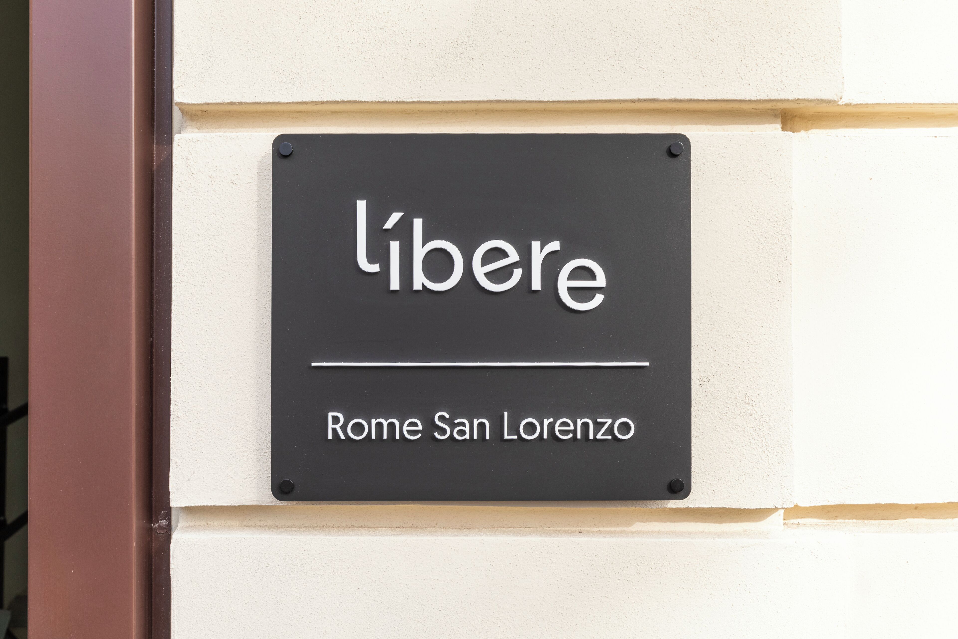 Une enseigne portant les noms « libere » et « Rome San Lorenzo » est fixée à la façade d’un immeuble.