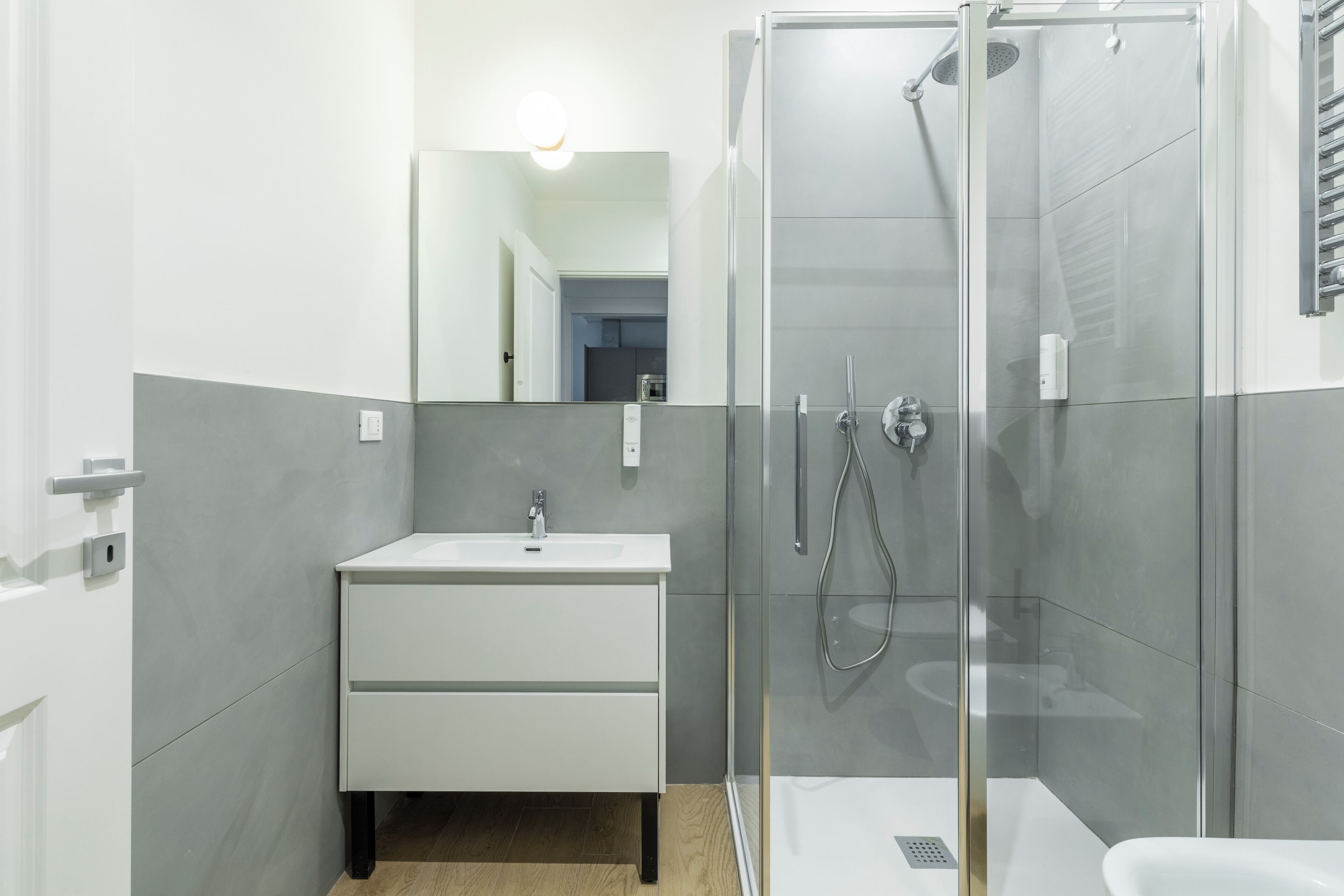 Ein modernes Badezimmer mit einer gläsernen Dusche, einem weißen Waschbecken und einem Spiegel.