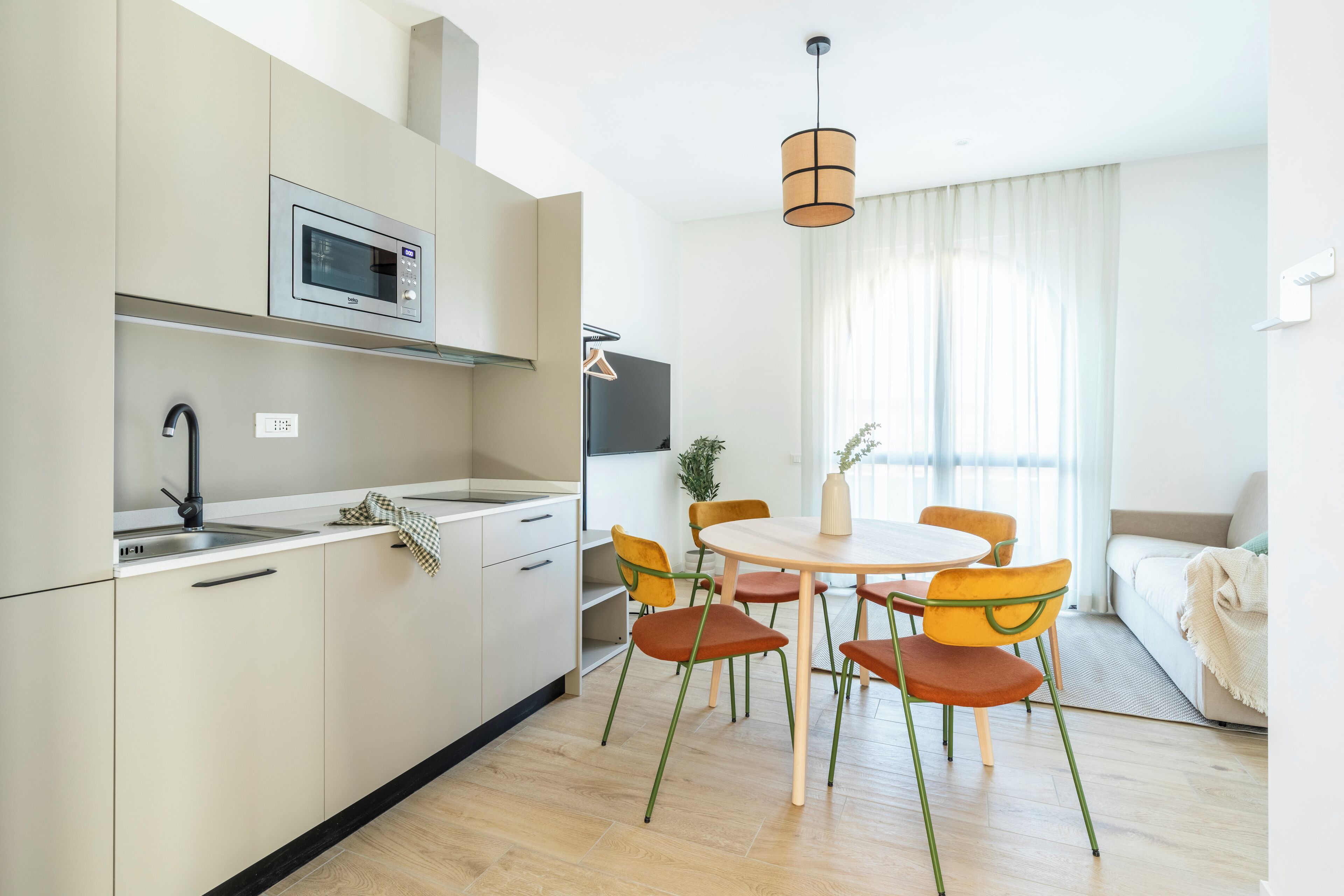 Une cuisine moderne équipée d’un four à micro-ondes, d’un évier et de placards. On y trouve également un coin repas avec une table ronde et quatre chaises. Une plante est visible à l’arrière-plan.