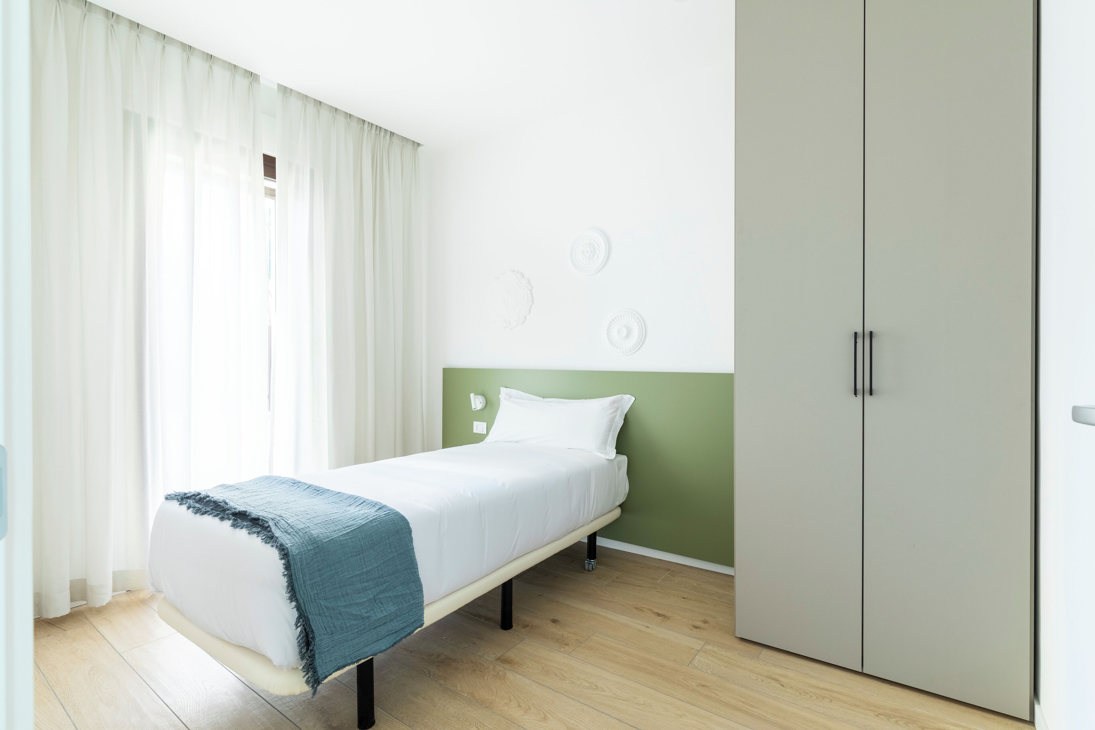 Un lit simple avec un matelas blanc et une couverture bleue, un mur d’accent vert et une armoire à deux portes.