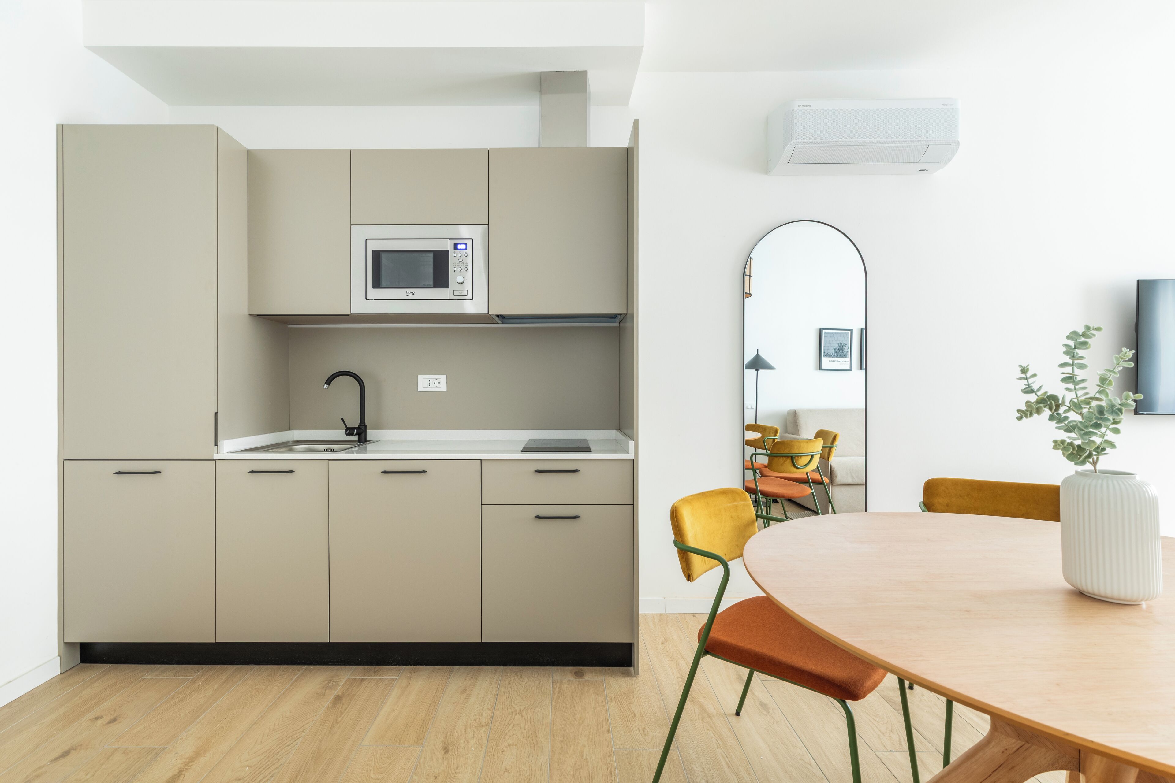 A modern kitchen with beige cabinets, a microwave, and a sink. There is a dining area with a wooden table and chairs.