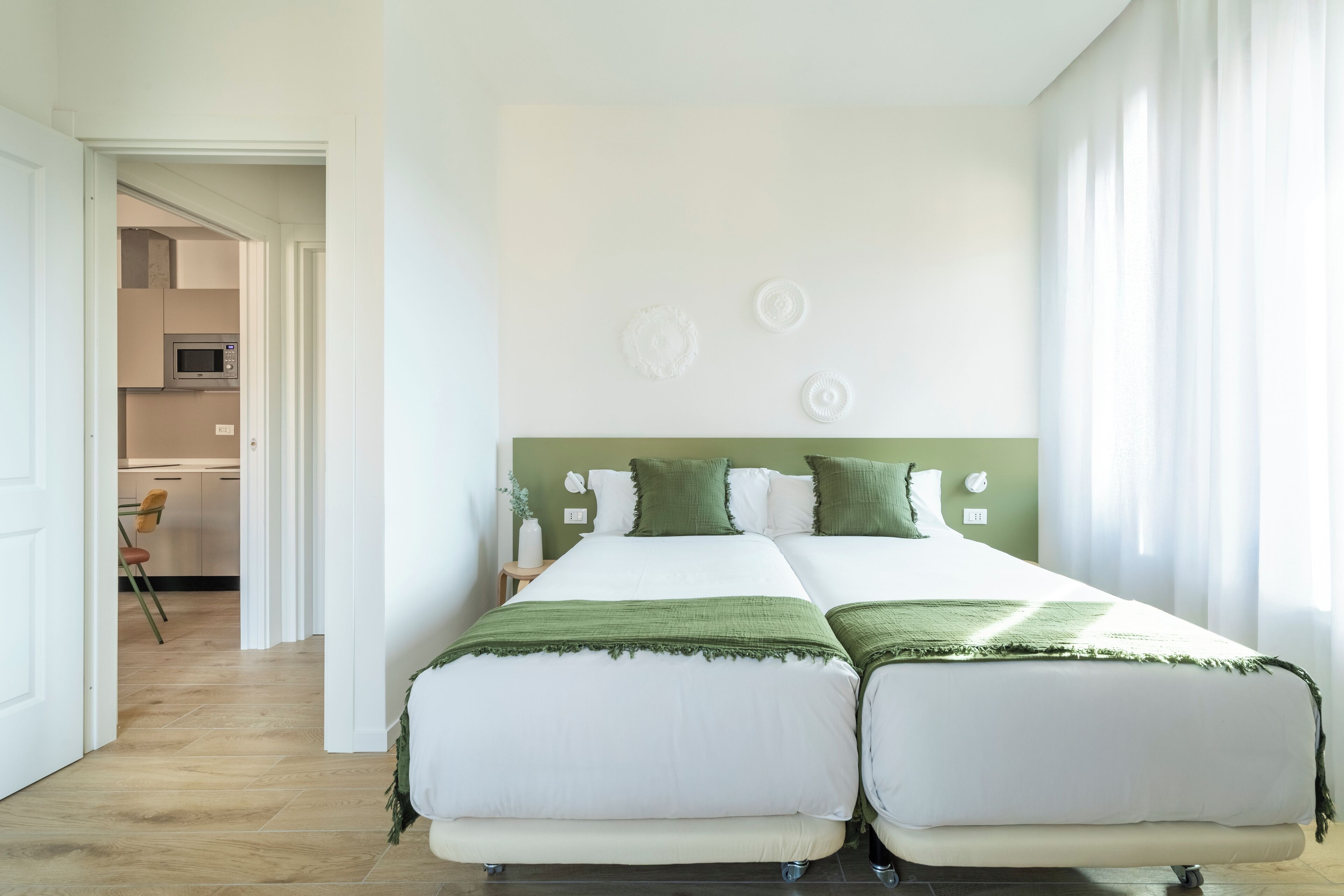 Ein Doppelbett mit grüner Bettwäsche, ein weißer Kopfteil und ein Blick auf eine Küche im Hintergrund.
