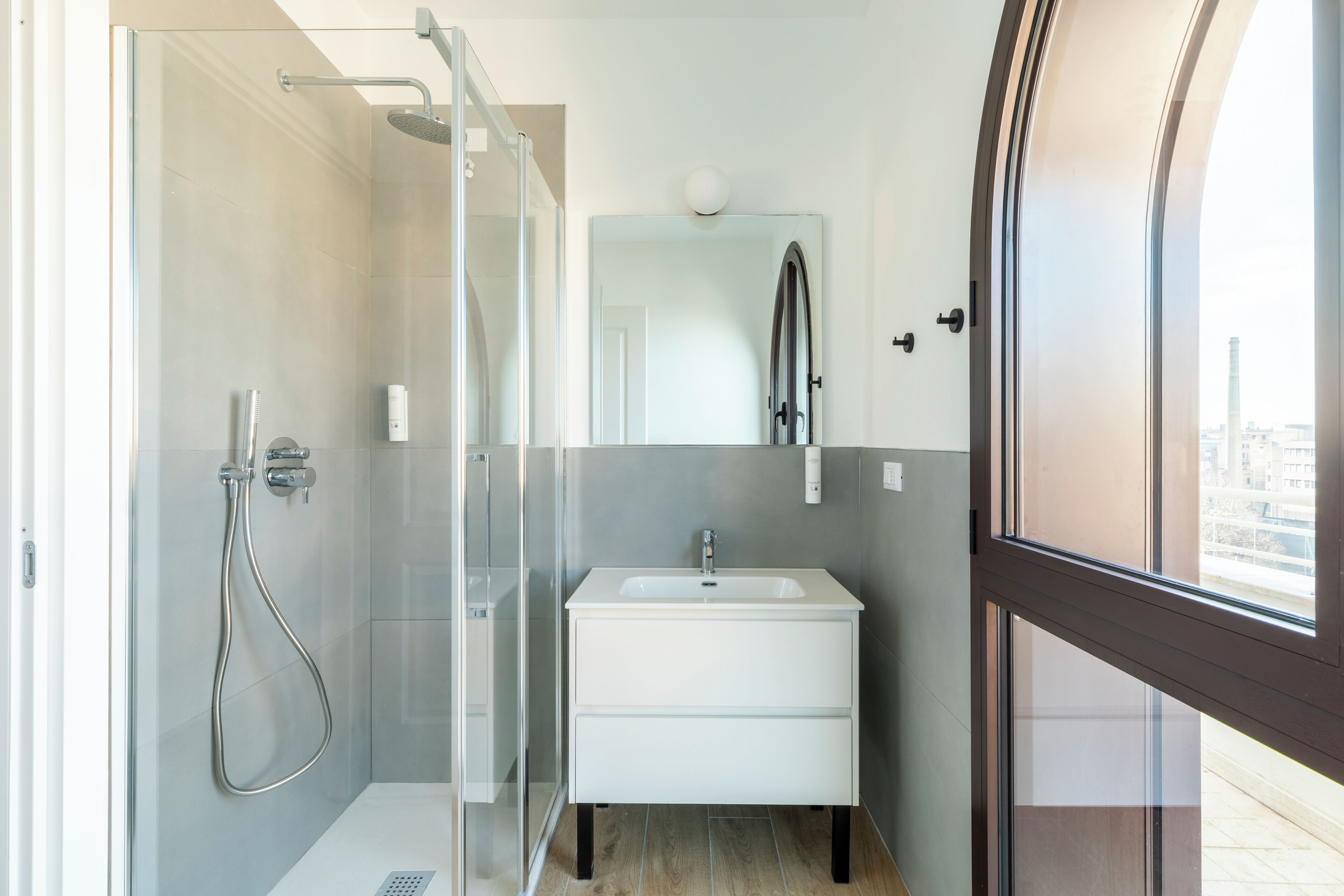 Un baño moderno con cabina de ducha de vidrio, un lavamanos blanco y un espejo encima.