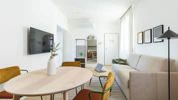 A modern living room with a beige sofa, a round wooden table, and a TV mounted on the wall.