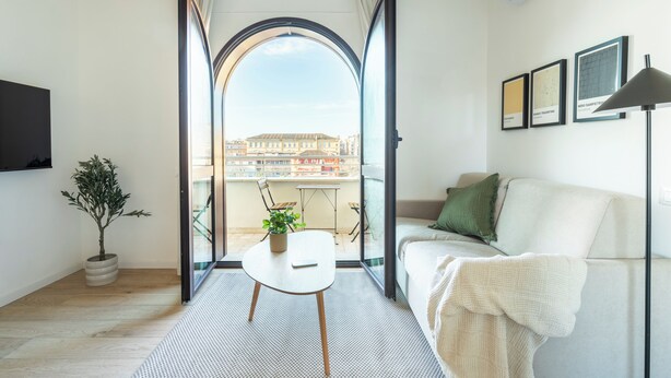 A modern living room with a sofa, a small table with a plant, and a view through an open archway to a balcony. - Líbere Rome San Lorenzo (Rome)
