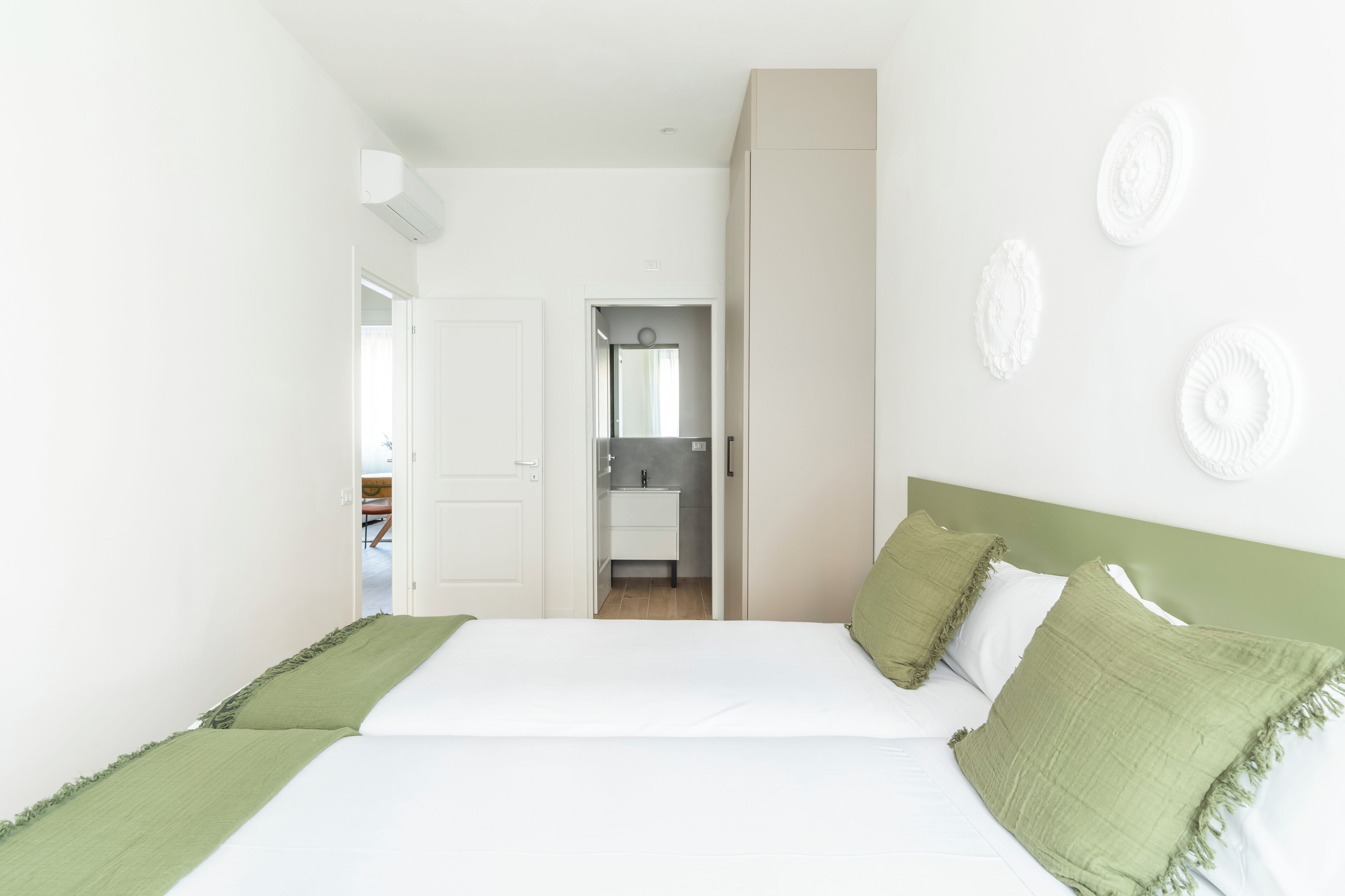 A bedroom with a bed, green pillows, a white headboard, and a view into the bathroom.