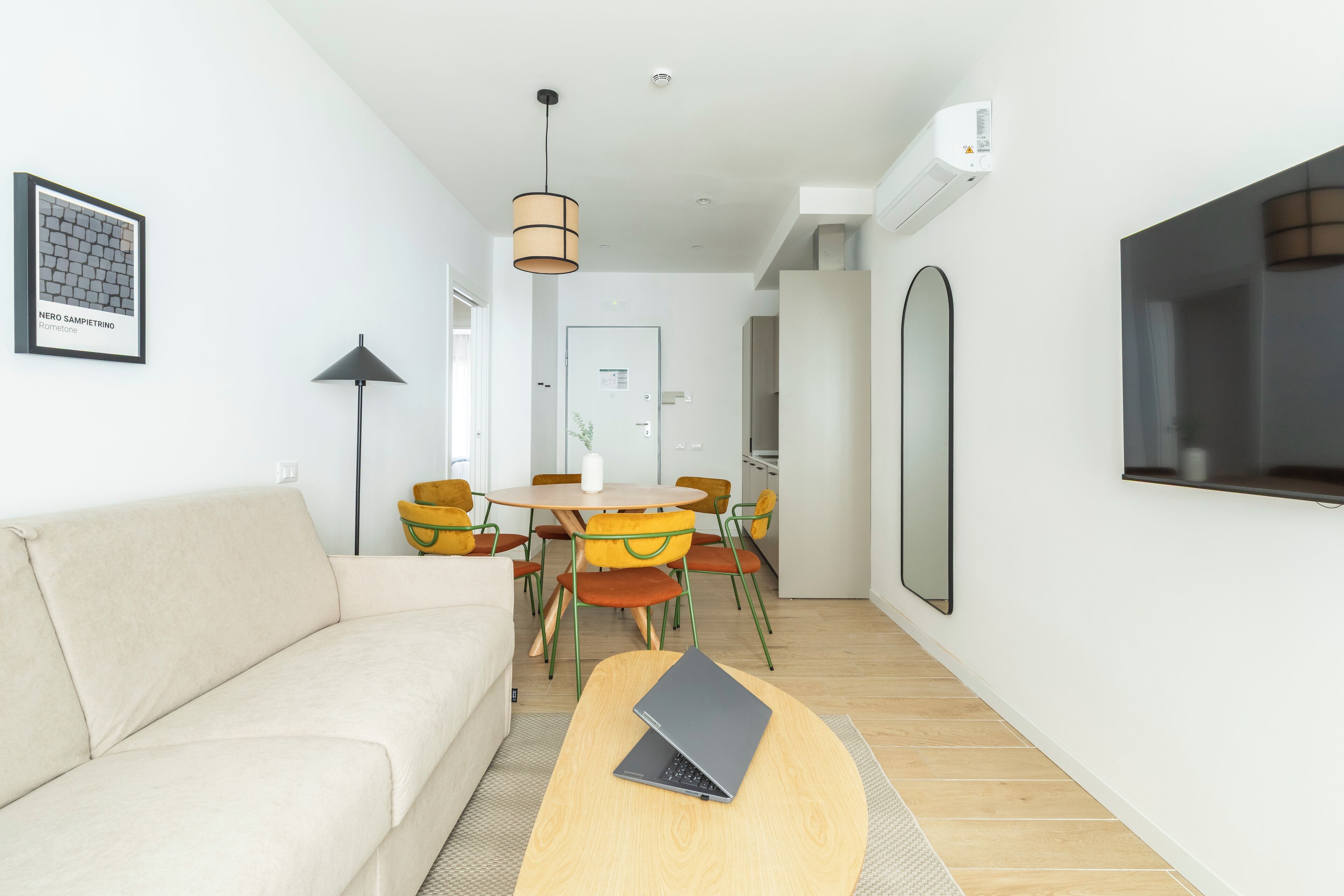 Un salon moderne comprenant un canapé, une table basse, une table à manger avec des chaises, un téléviseur et un appareil de climatisation.