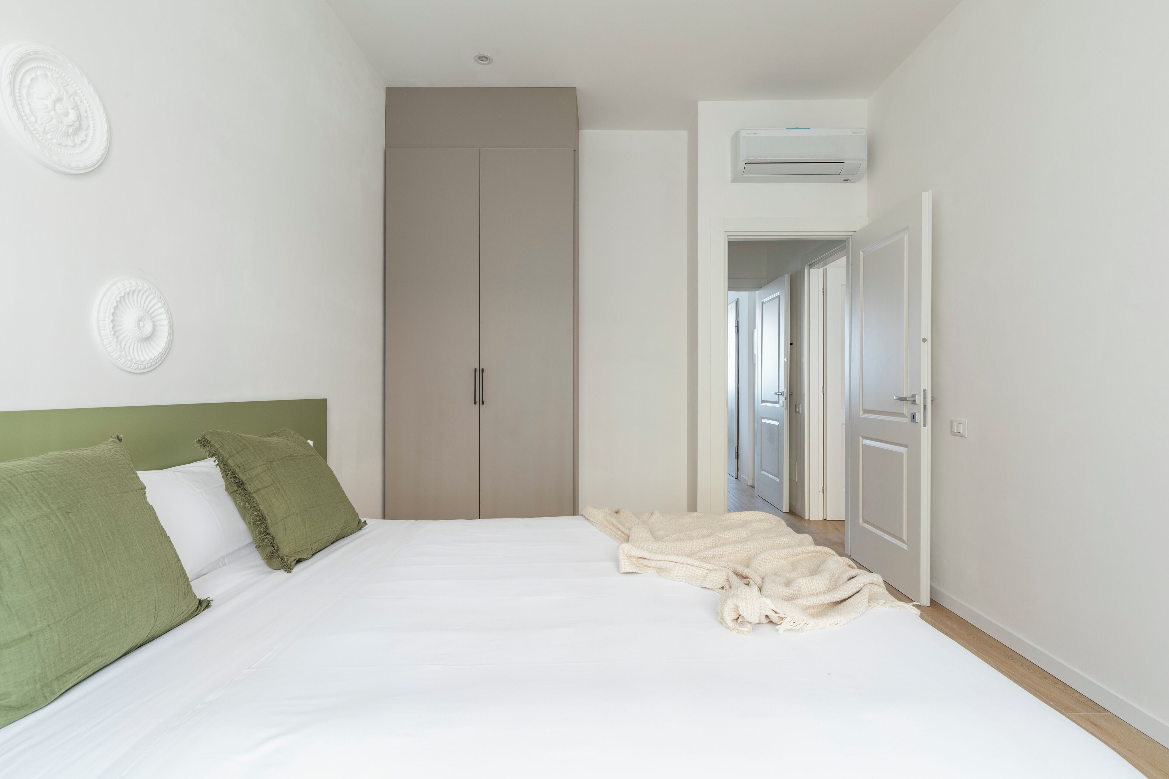 Ein Schlafzimmer mit einem Bett, grünen Kissen, einer beigen Decke, einem Kleiderschrank und einer Klimaanlage.