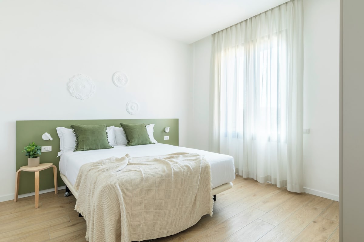 A bedroom with a bed, a bedside table with a plant, and a window with curtains.