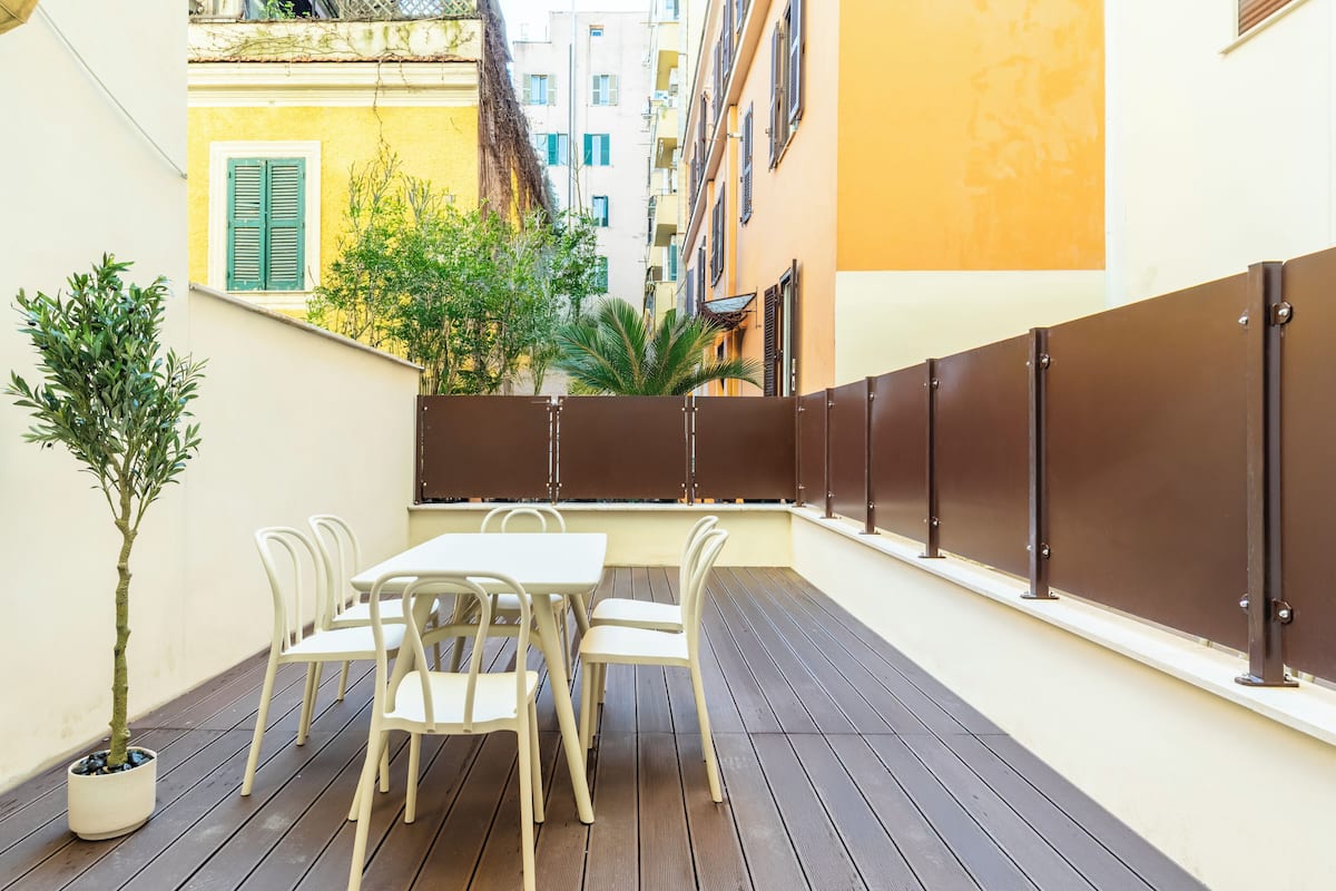 An outdoor patio with a table and chairs, a potted plant, and a view of adjacent buildings.