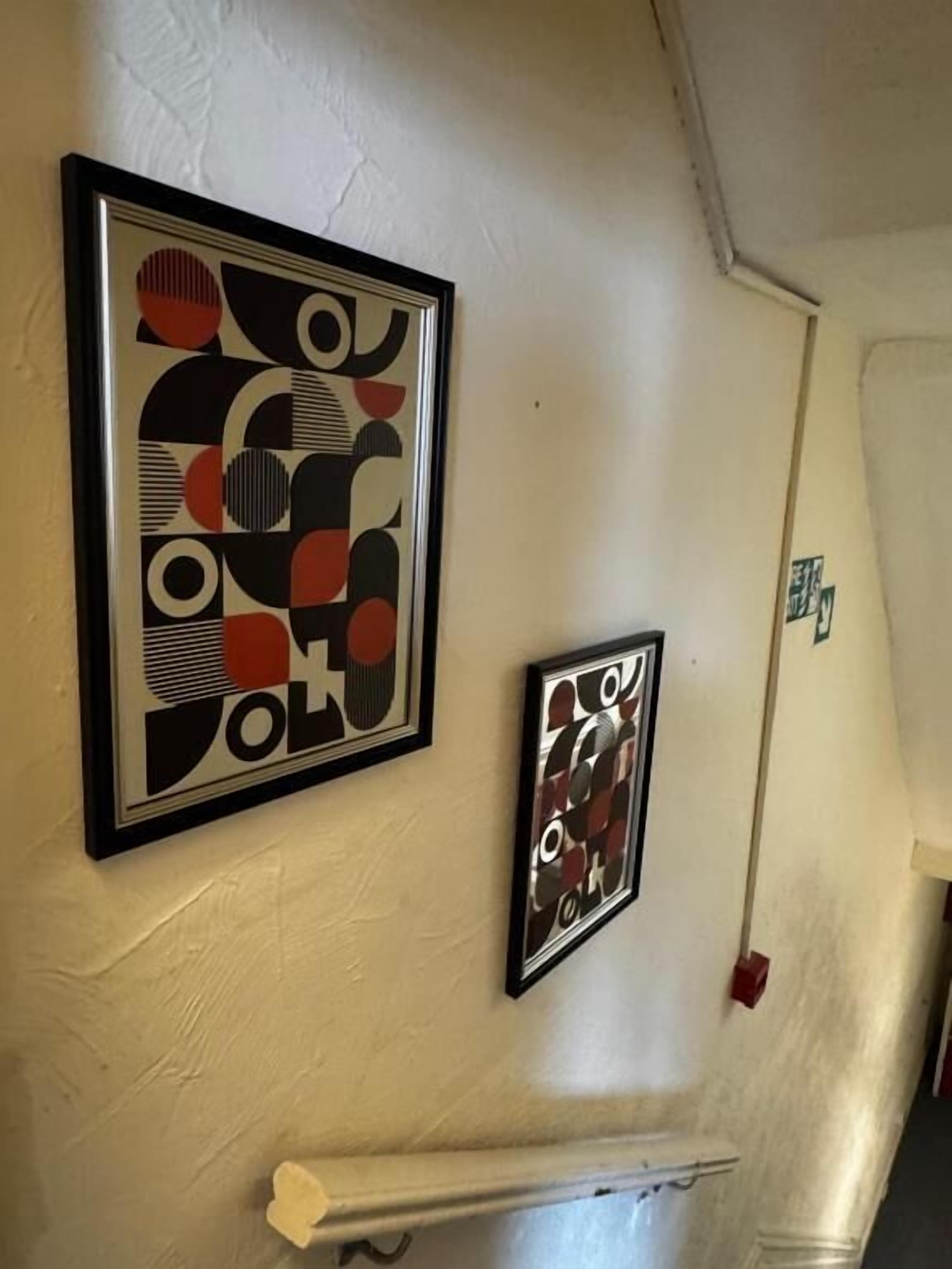 Two abstract art pieces on a plain wall.