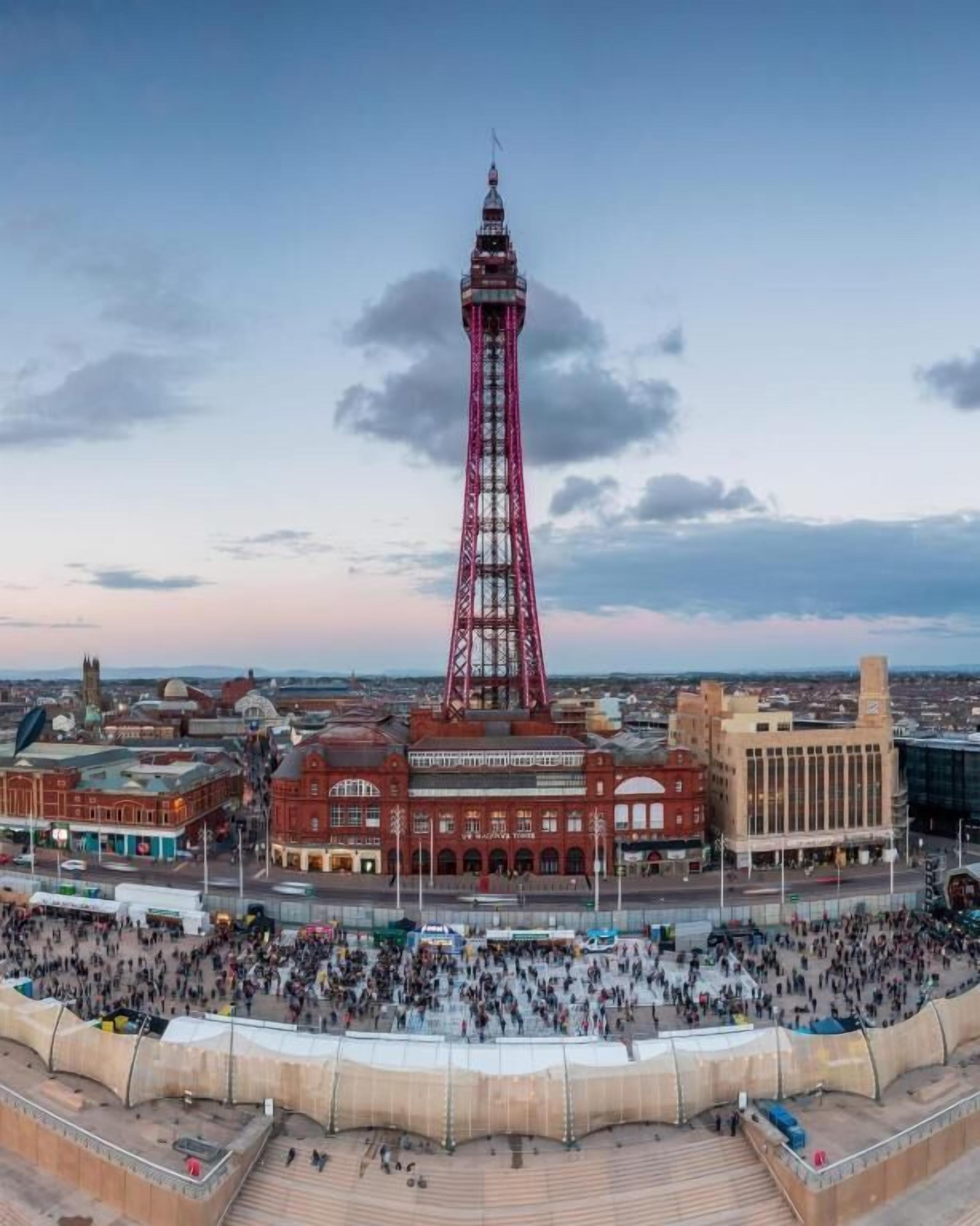A large public square with a prominent tower in the center, surrounded by historic buildings and a crowd of people.