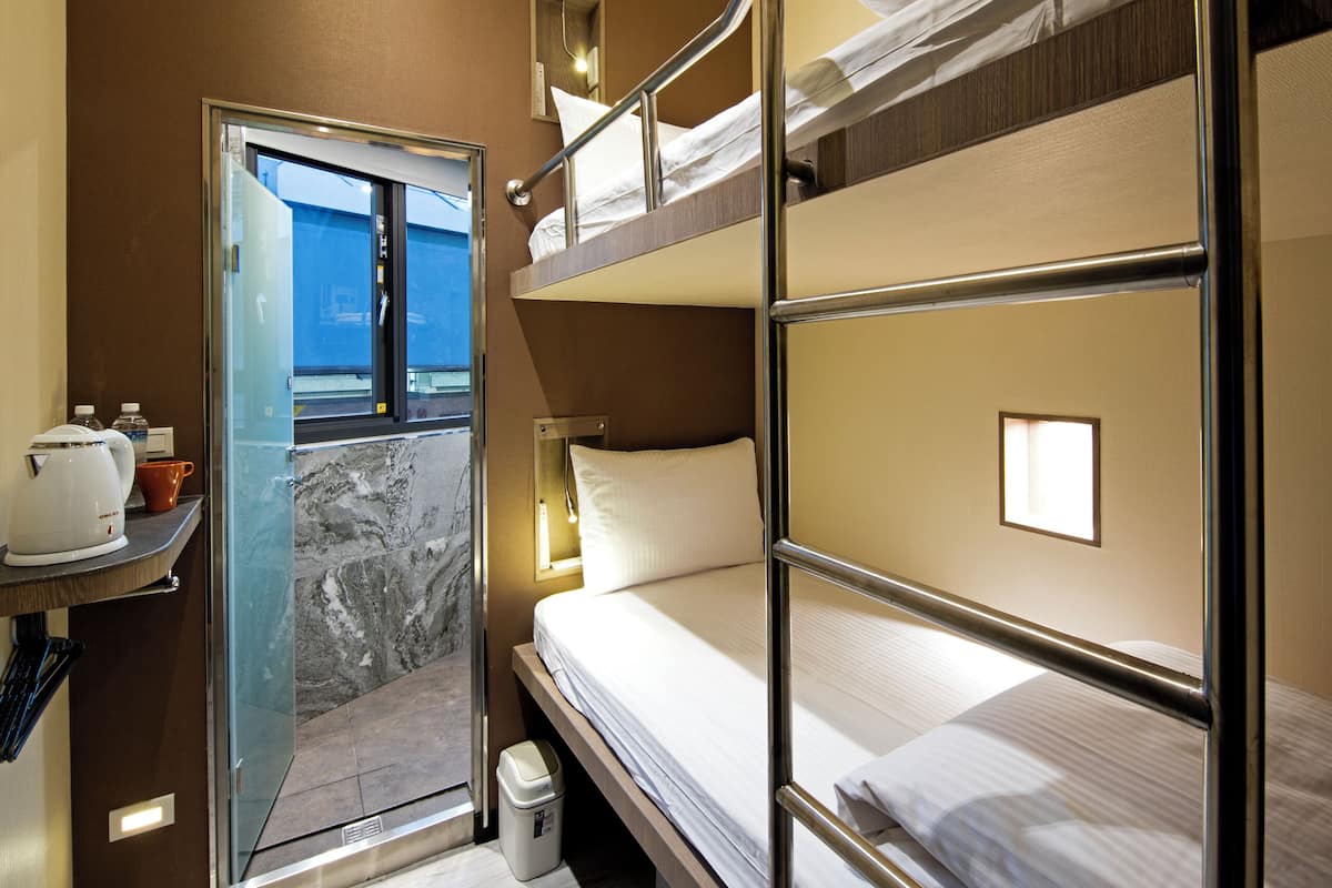 A compact hotel room with bunk beds, a small kitchenette, and a view through a door.