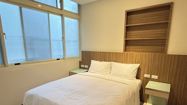 A modern bedroom with a large bed, a nightstand, a wooden headboard, and a window with frosted glass. - 35APT- Self Check In (Taipei)