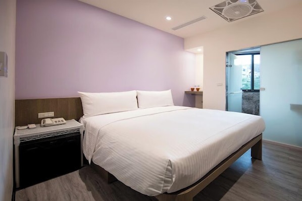 Quarto com cama, mesa de cabeceira com telefone e uma pequena estante com objetos decorativos.