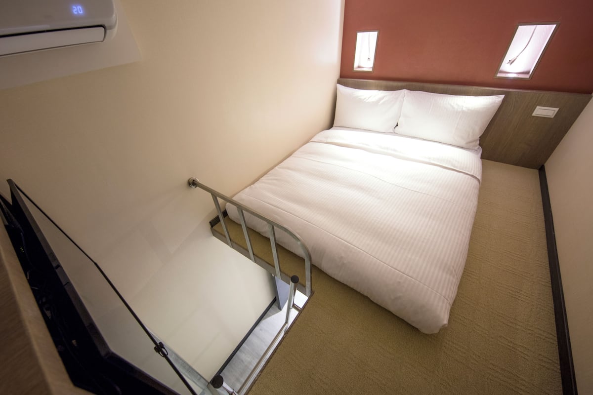 A hotel room with a bed, a small table, and a window.