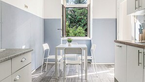 Une cuisine de taille réduite avec une fenêtre, des placards blancs et une table à manger avec des chaises.