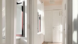 Un couloir étroit avec des portes blanches, un radiateur et une fenêtre donnant sur un mur rouge.