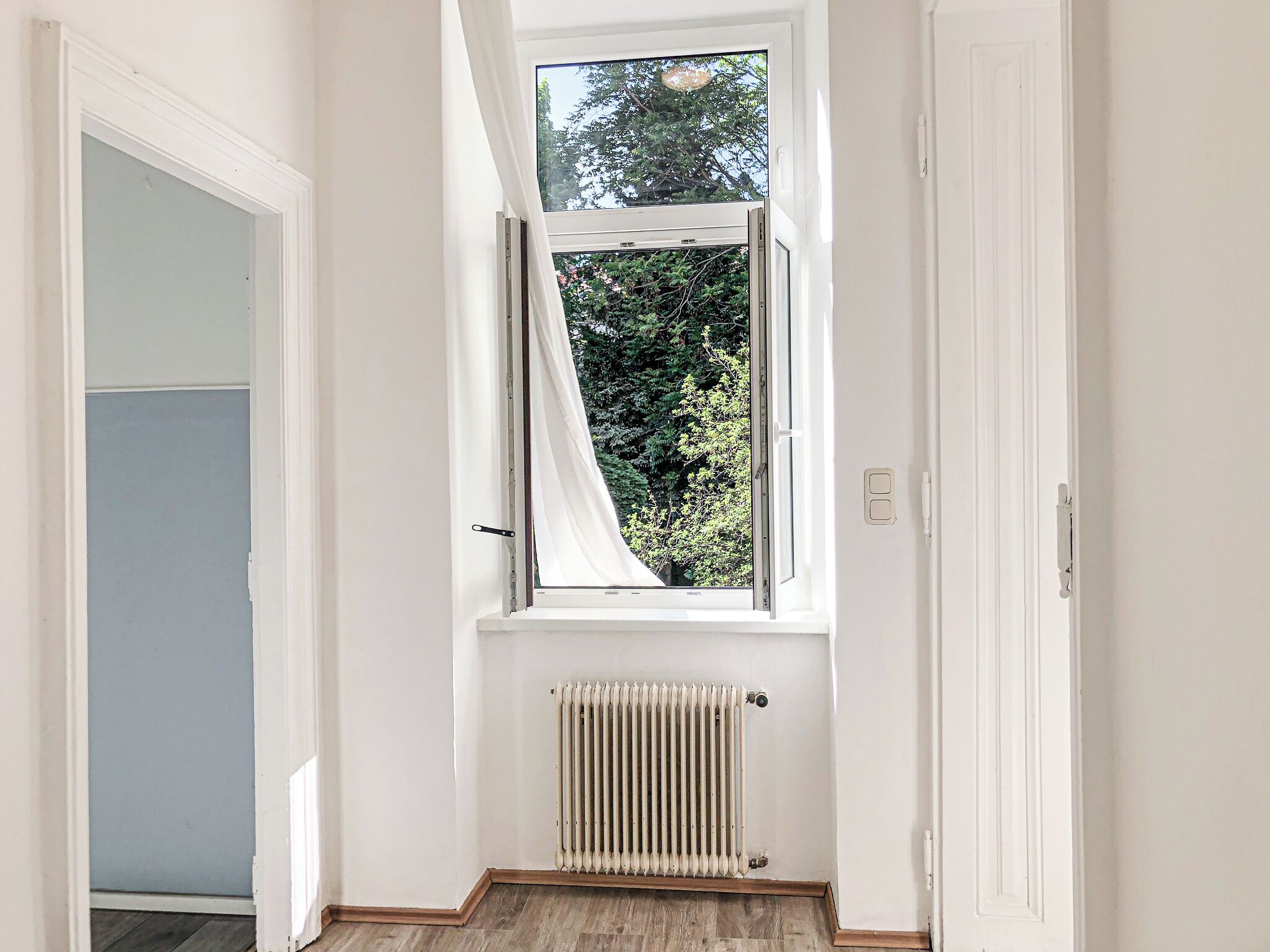 Een smalle gang met een raam, een radiator en een deur.