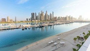 A marina with boats docked, a sandy beach with umbrellas, and a city skyline in the background. - StayShort - Elegant 1 Bedroom in EMAAR Beachfront that Sleeps 2 (EMAAR Beachfront)