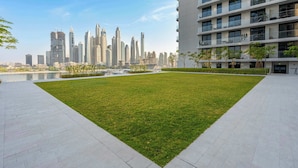 A modern building with a courtyard featuring a well-maintained lawn and a water body in the background. - StayShort - Elegant 1 Bedroom in EMAAR Beachfront that Sleeps 2 (EMAAR Beachfront)