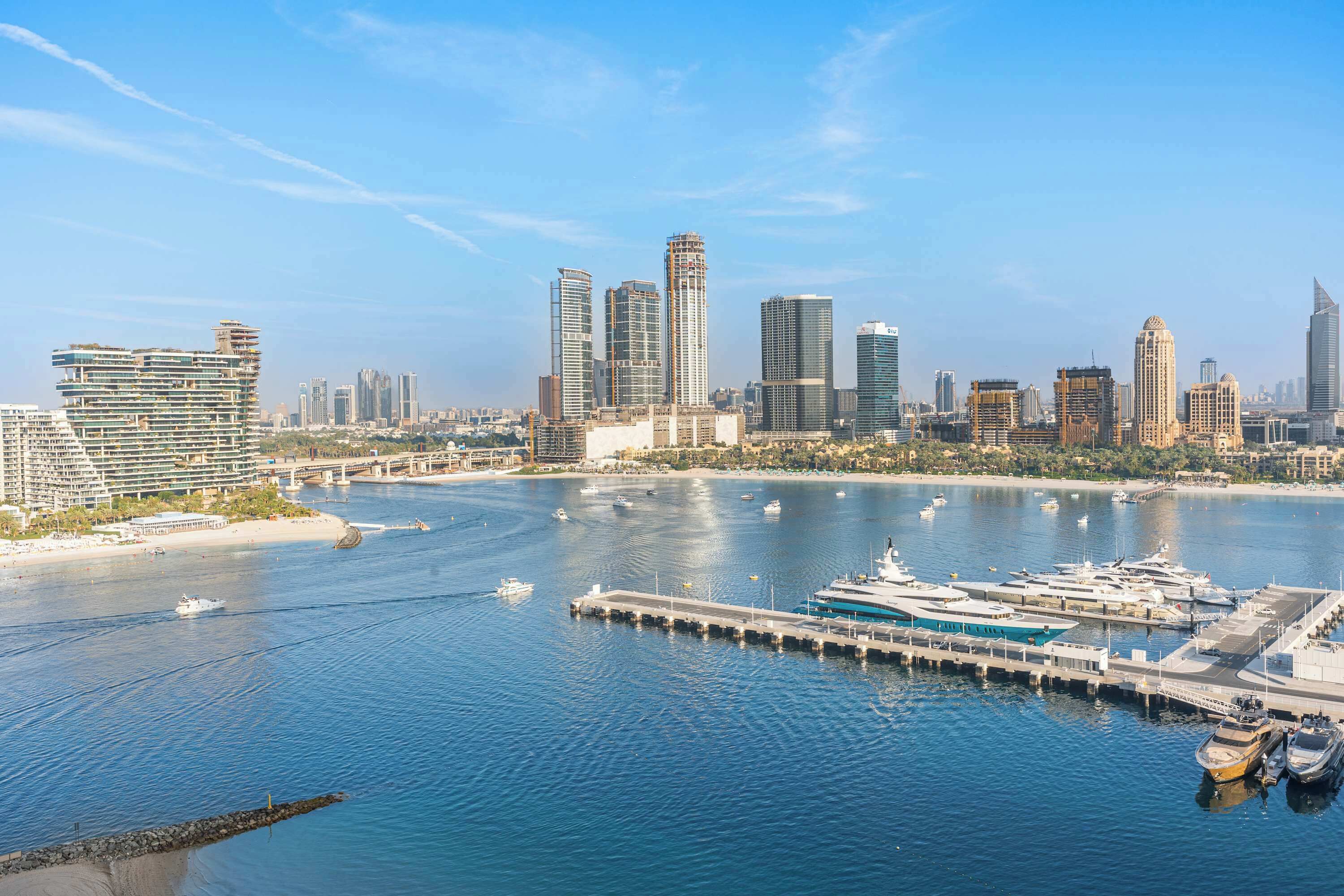 A marina with yachts docked, a bridge, and a city skyline with modern skyscrapers.