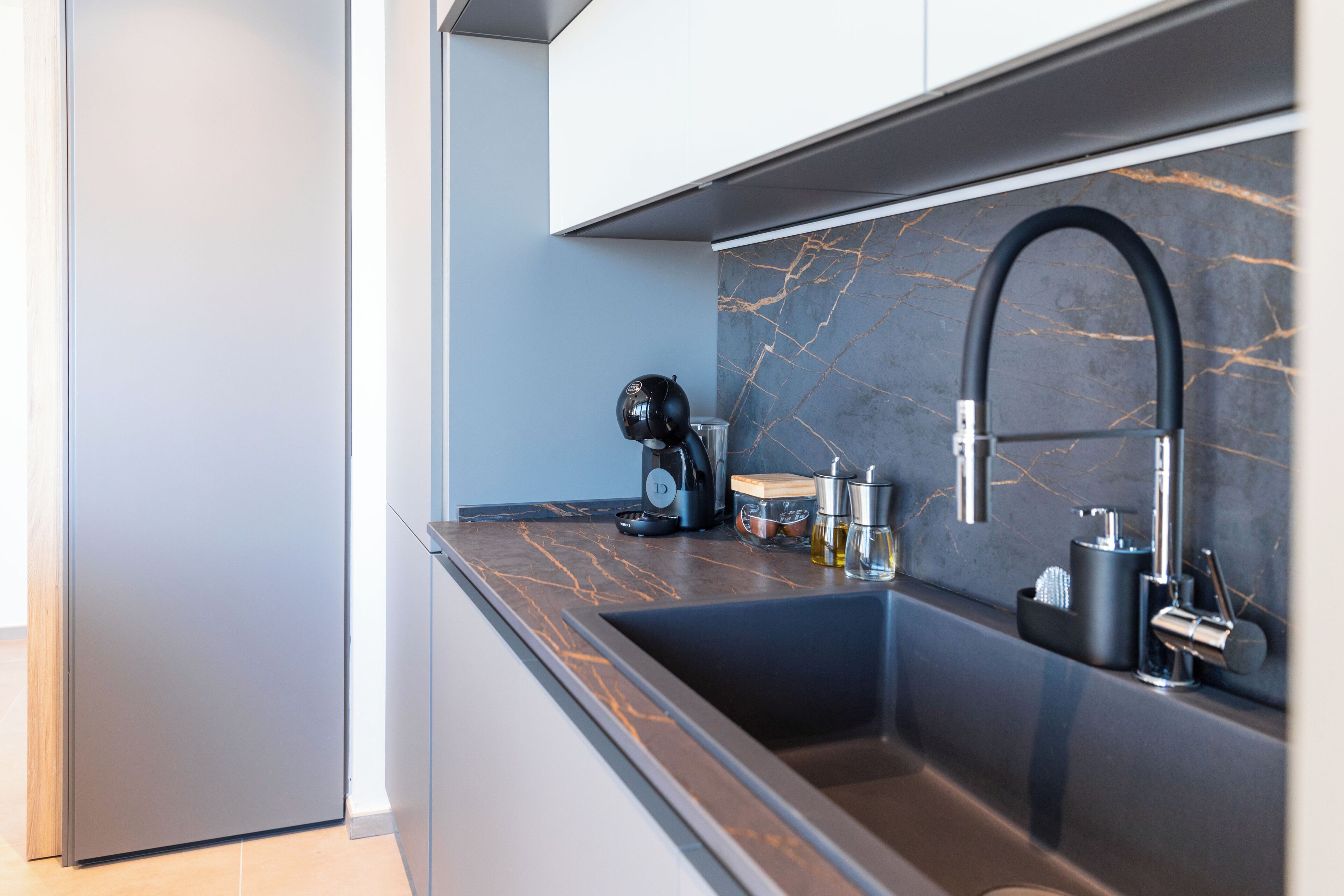 A modern kitchen with a dark marble backsplash, a black sink, and stainless steel appliances.
