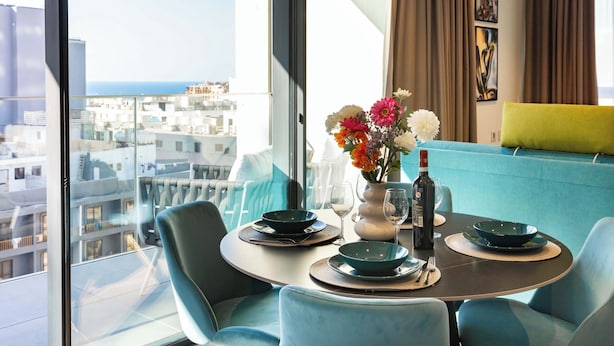 A dining area with a table set for two, a vase of flowers, and a bottle of wine. - Mercury Tower (St. Julian's)