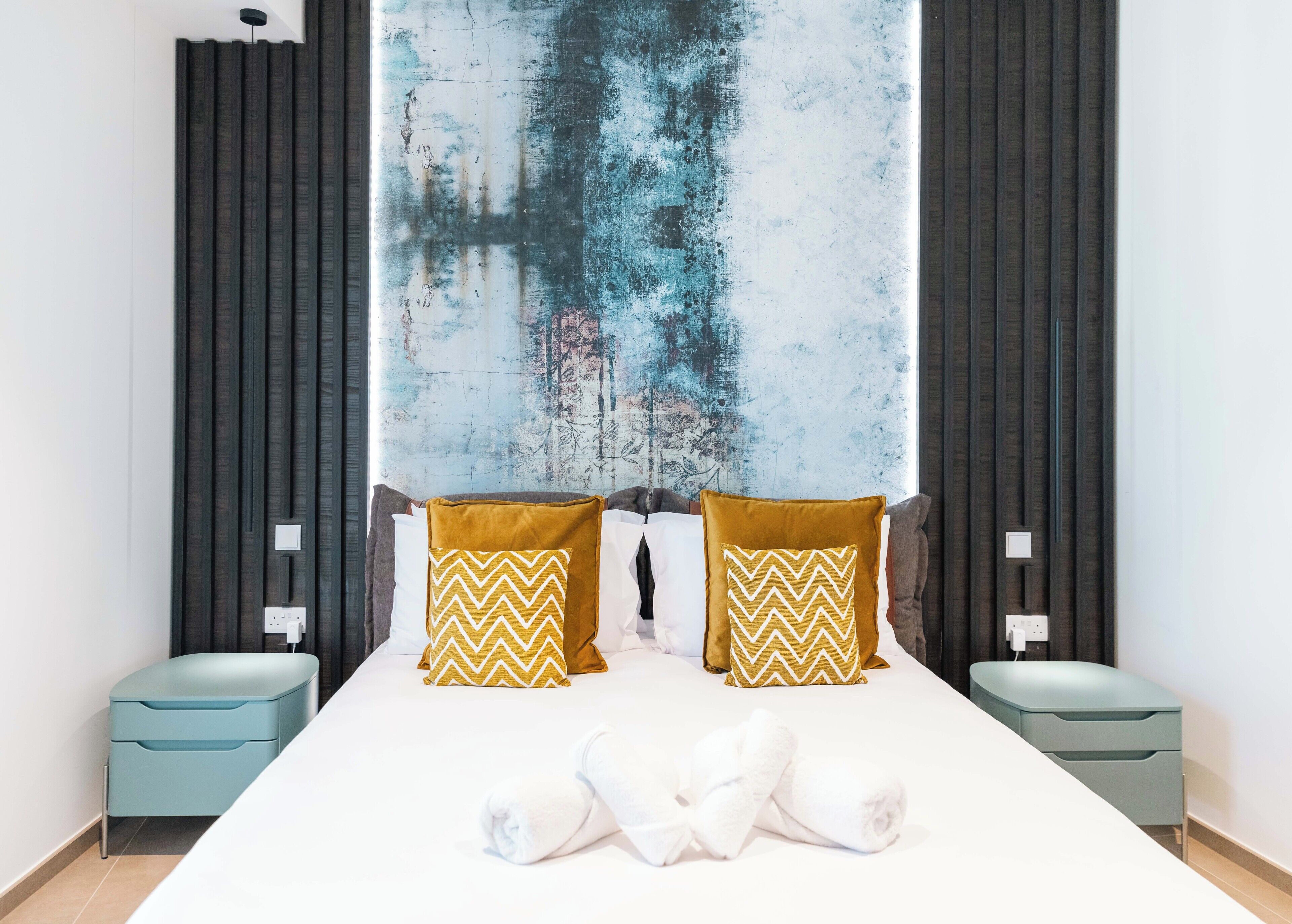 Une chambre d’hôtel avec un grand lit, deux tables de chevet et un grand tableau abstrait accroché au mur.