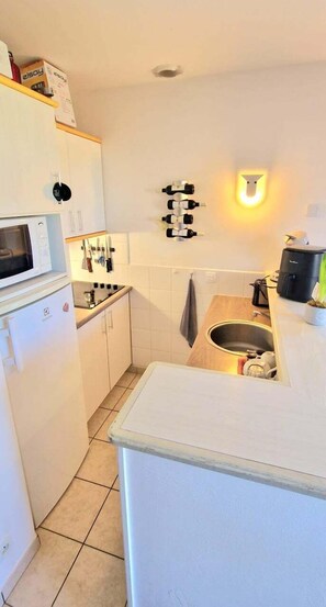 Een kleine keuken met een magnetron, een spoelbak en een aanrecht met een koffiezetapparaat.