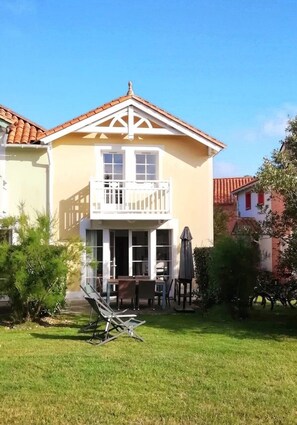 Een tweelaags huis met een balkon, een terras met tafel en stoelen, en een gazon.