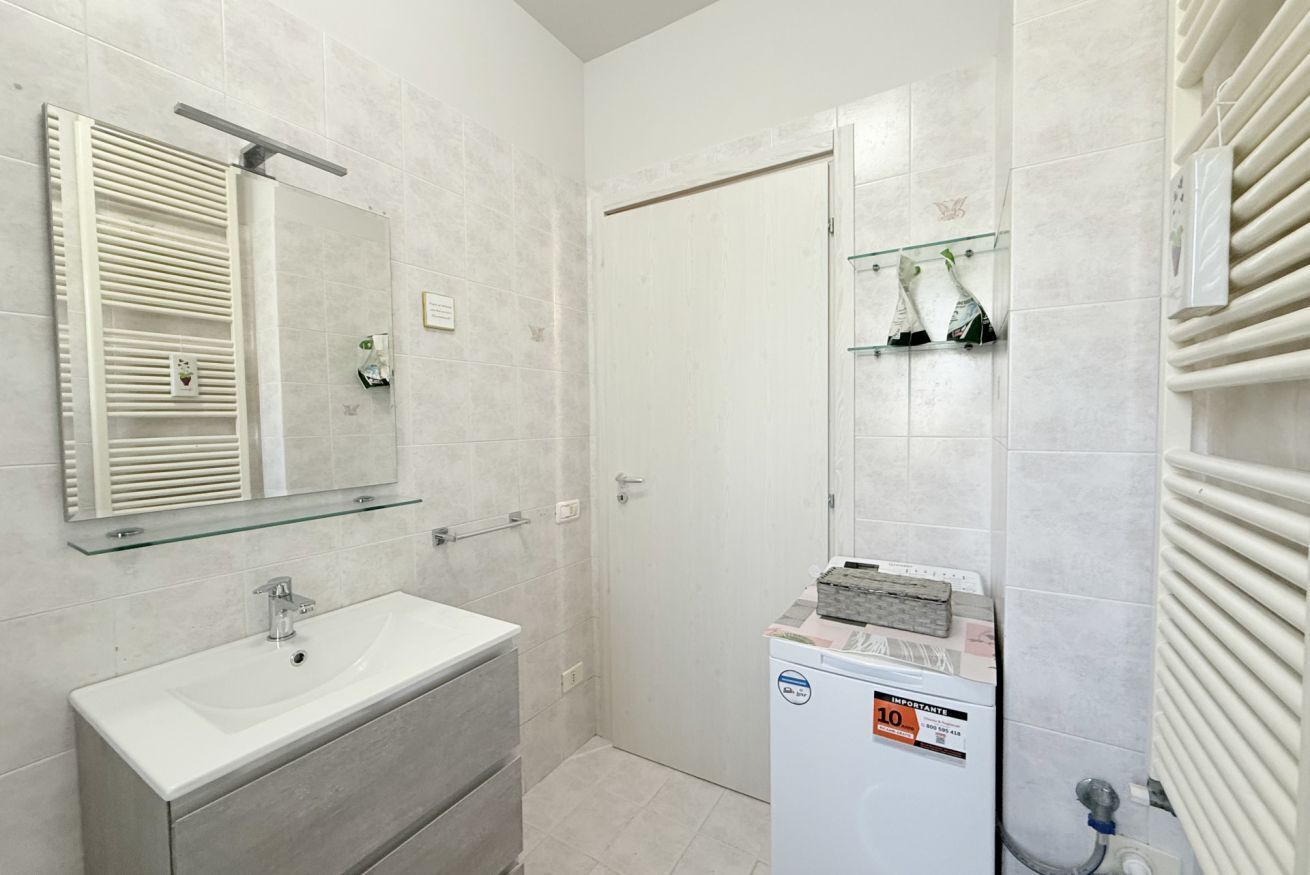 A bathroom with a white sink, a glass shelf, a mirror, a shower, and a white radiator.