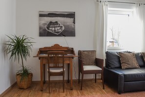 A room with a wooden desk, two chairs, a black sofa, a potted plant, and a painting of a boat on water.