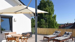 An outdoor deck with a table and chairs, a sun lounger, and a large umbrella. - Holiday Apartment Im Weiler, 70m², 1 Bedroom, Up to 4 Guests (Winterlingen)